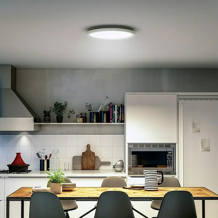 Philips Hue LED-Panel rund White Ambience Aurelle - 21 W, Ø x H: 39,5 x 4,7 cm, Weiß, Warmweiß - Eine moderne, runde Deckenleuchte erhellt eine stilvolle Küche mit Esstisch und weißen Möbeln. Sie sorgt für eine angenehme Atmosphäre.