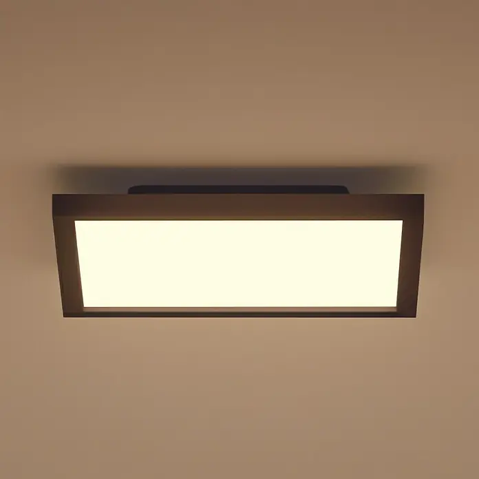 Philips Hue LED-Panel White Ambience Aurelle - 19 W, L x B x H: 30 x 30 x 4,6 cm, Schwarz, Warmweiß - Nahaufnahme einer modernen Deckenleuchte mit rechteckigem, schwarzem Rahmen und warmweißem Licht, die an einer hellbraunen Decke montiert ist.