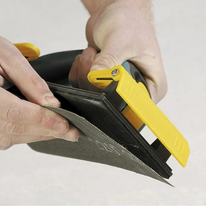 Wolfcraft Set malla abrasiva - An x L: 115 x 280 mm - Primer plano de una lijadora de mano con mango amarillo cargando papel de lija, ideal para aplicaciones de lijado de superficies.