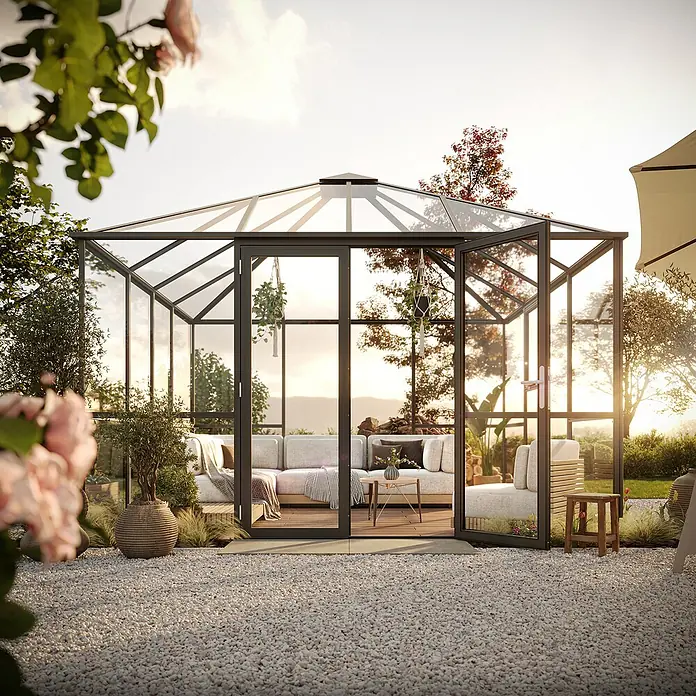 KGT Gewächshaus PaviLux 3,5 - Außenmaß inkl. Dachüberstand (B x T): 350 x 350 cm, 4 mm, Anthrazit-grau, Einscheibensicherheitsglas - Elegantes Gartenhaus mit Glaswänden und schwarzem Rahmen, eingerichtet mit einer komfortablen Couch und stilvollen Dekorationen für entspannte Stunden im Freien.