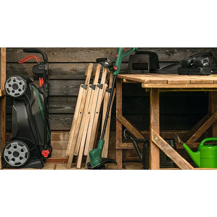 Bosch Power for All 18V Akku-Rasenmäher ROTAK18V2-43 - Ohne Akku, Schnittbreite: 43 cm - Eine Nahaufnahme eines Rasenmähers, Trimmers und anderer Gartengeräte, die ordentlich in einem Schuppen aufbewahrt werden.