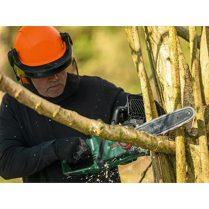 Bosch Power for All 18V Akku-Kettensäge PKE18V-30-28 - 18 V, 4 Ah, Li-Ionen, 1 Akku, Schwertlänge: 30 cm - Ein Mann sägt mit einer Bosch Akku-Kettensäge einen Ast. Er trägt Schutzkleidung für sicheres Arbeiten mit der Kettensäge.