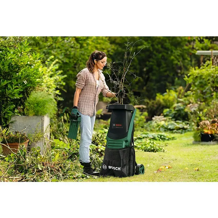 Bosch Power for All 18V Akku-Häcksler UniversalShredder 2x18V-25 - Max. Aststärke: 25 mm - Frau benutzt einen Bosch Gartenhäcksler, um Gartenabfälle zu zerkleinern. Das Gerät ist grün und schwarz und hat einen Auffangsack.