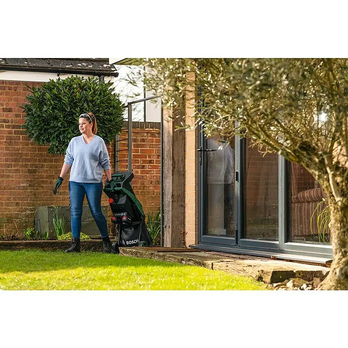 Bosch Power for All 18V Akku-Häcksler UniversalShredder 2x18V-25 - Max. Aststärke: 25 mm - Eine Frau zieht einen Bosch Gartenhäcksler im Garten. Das Gerät ist schwarz und grün.