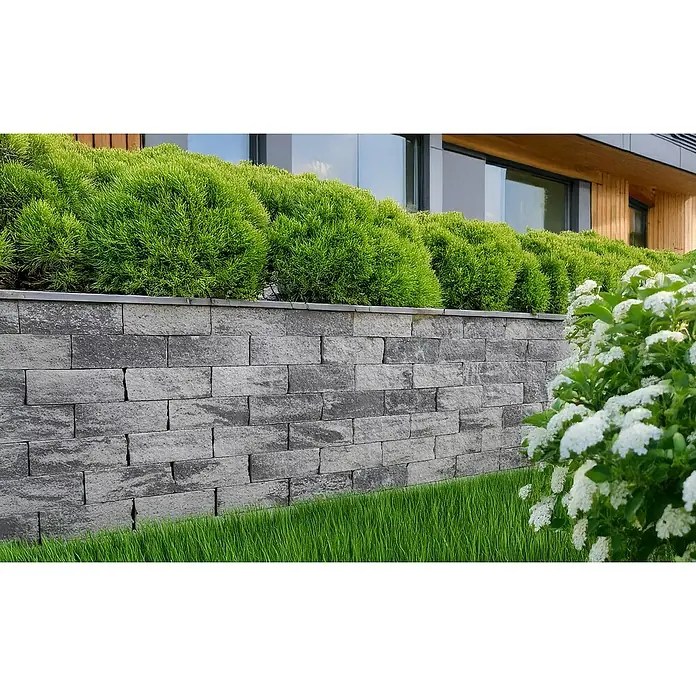EHL EIBA Mauerstein - 30 x 15 x 12 cm, Grau-Anthrazit, Beton - Eine graue Steinmauer mit grünen Büschen darauf, die ein modernes architektonisches Element hervorhebt. Perfekt für Gärten und Außenbereiche.