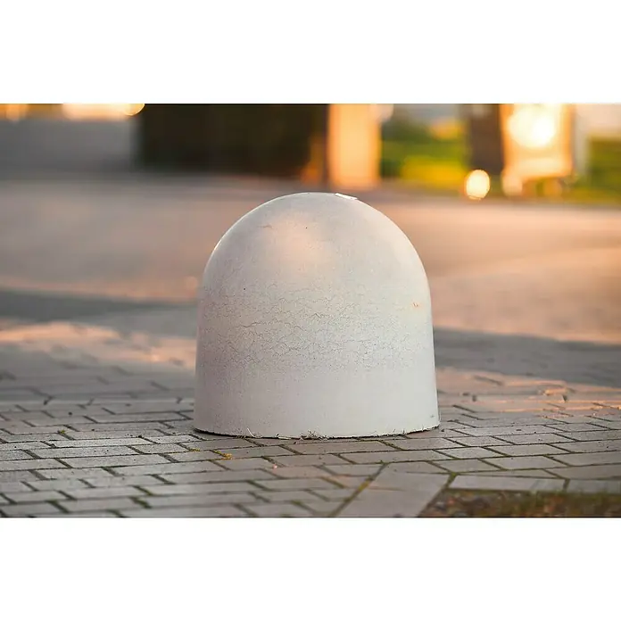 Diephaus Poller Rund - Ø x H: 50 x 50 cm, Grau, Beton - Nahaufnahme eines runden, weißen Betonpoller auf einem gepflasterten Weg, der bei sanftem, goldenem Licht Schutz bietet.