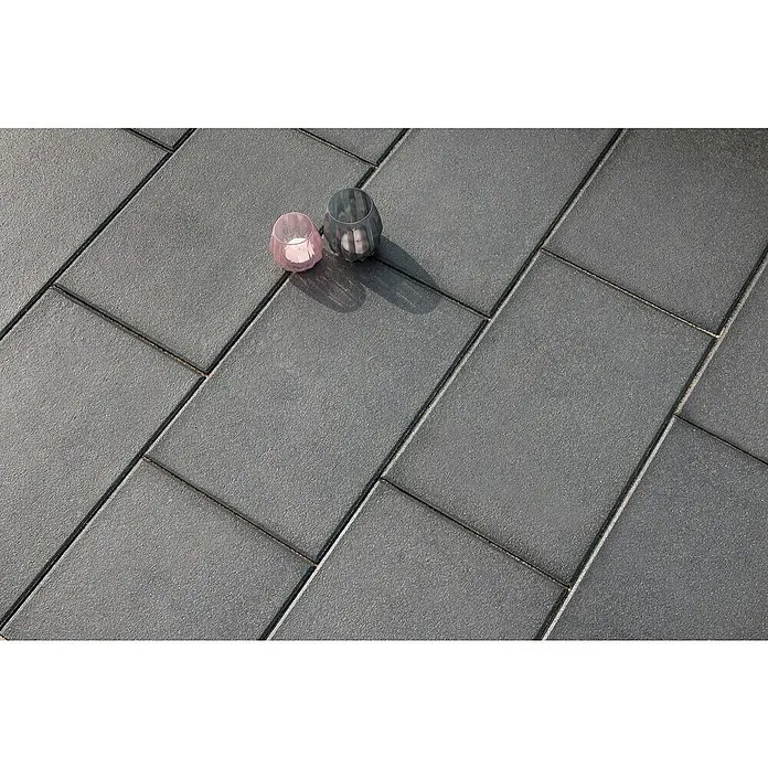 Diephaus Terrassenplatte Redding - 60 x 30 x 4 cm, Schwarz-Basalt, Beton - Graue Pflastersteine mit zwei Kerzenhaltern. Das Bild zeigt die Struktur und das Muster der Steine für den Außenbereich.