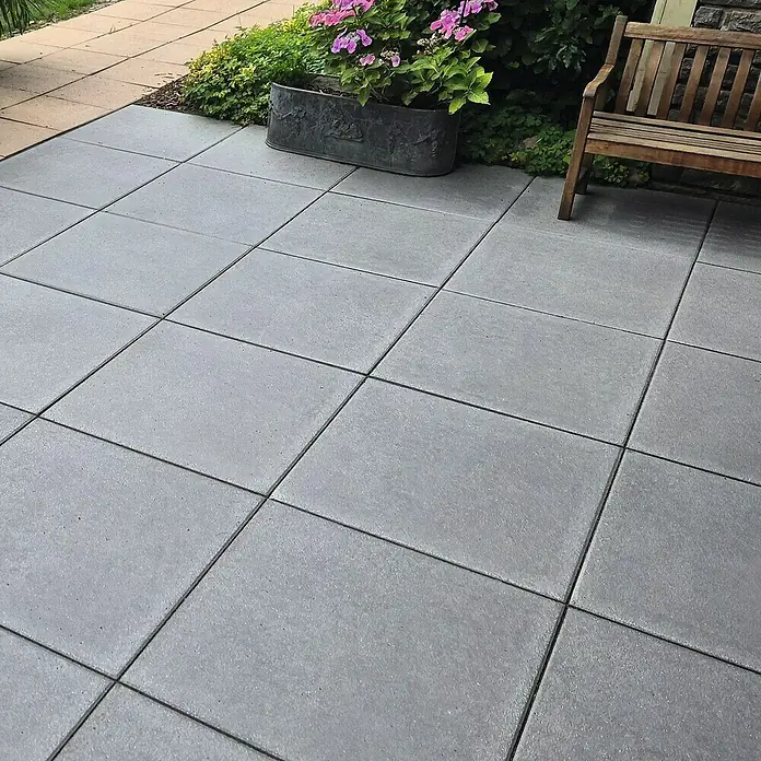 Diephaus Terrassenplatte Redding - 60 x 60 x 4 cm, Quarz, Beton - Gepflasterte Terrasse mit grauen quadratischen Pflastersteinen, einem Blumenkasten mit rosa Blüten und einer Holzbank im Hintergrund.