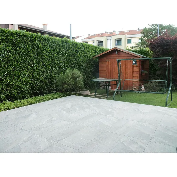 Terrassenfliese Quarzo Silver - 40 x 80 x 2 cm, Silber, Matt - Eine Gartenszene mit einer grauen Terrasse, einem Schuppen, einer Schaukel und üppigem Grün.