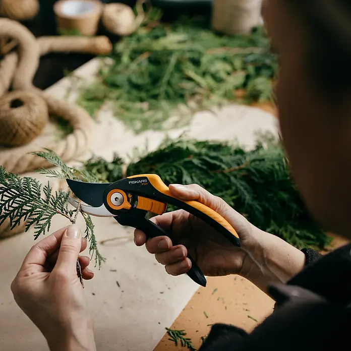 Fiskars Plus Gartenschere P541 - Bypass, Max. Aststärke: 24 mm - Eine Person schneidet einen kleinen Ast mit einer gelb-schwarzen Fiskars Gartenschere vor einem Hintergrund aus grünen Zweigen.