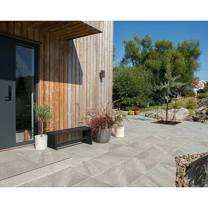 Terrassenfliese Quarzo Tortora - 60 x 60 x 2 cm, Grau/Braun, Matt - Einladende Terrasse mit stilvollen grauen Fliesen, die sich nahtlos in die moderne Architektur und die grüne Umgebung einfügen.