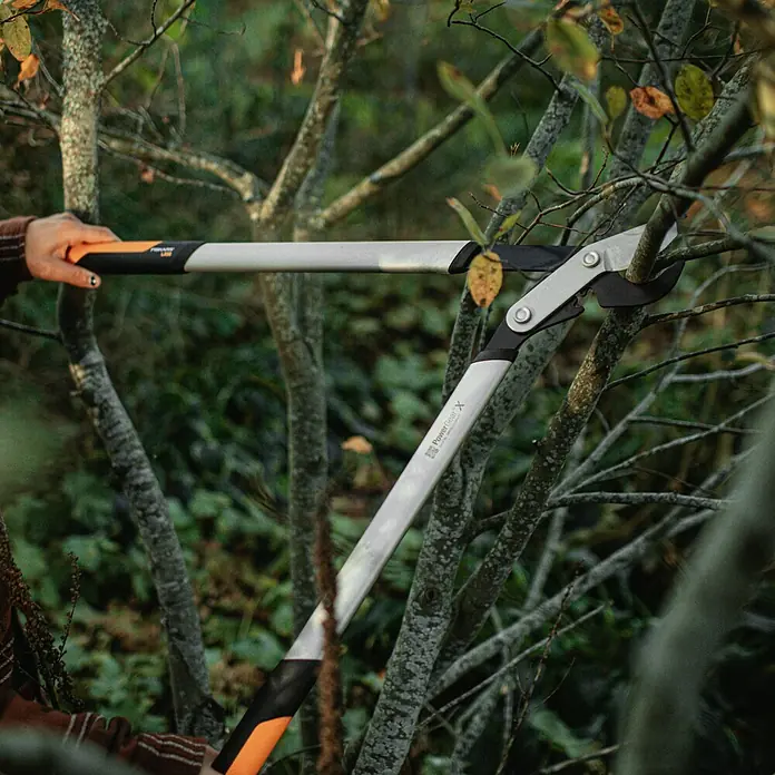 Fiskars Getriebe-Astschere PowerGearX LX98-L - Max. Aststärke: 50 mm, 80 cm - Nahaufnahme einer PowerGear X Astschere von Fiskars, die zum Beschneiden von Ästen in einem Garten verwendet wird.