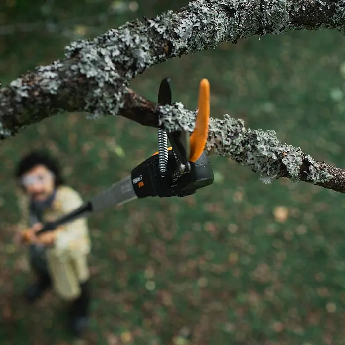 Fiskars Teleskop-Schneidgiraffe UPX86 - Max. Aststärke: 32 mm - Nahaufnahme einer Fiskars-Astschere im Einsatz an einem Baum, bedient von einer Person im Hintergrund. Ideal für Gartenarbeit und Baumpflege.