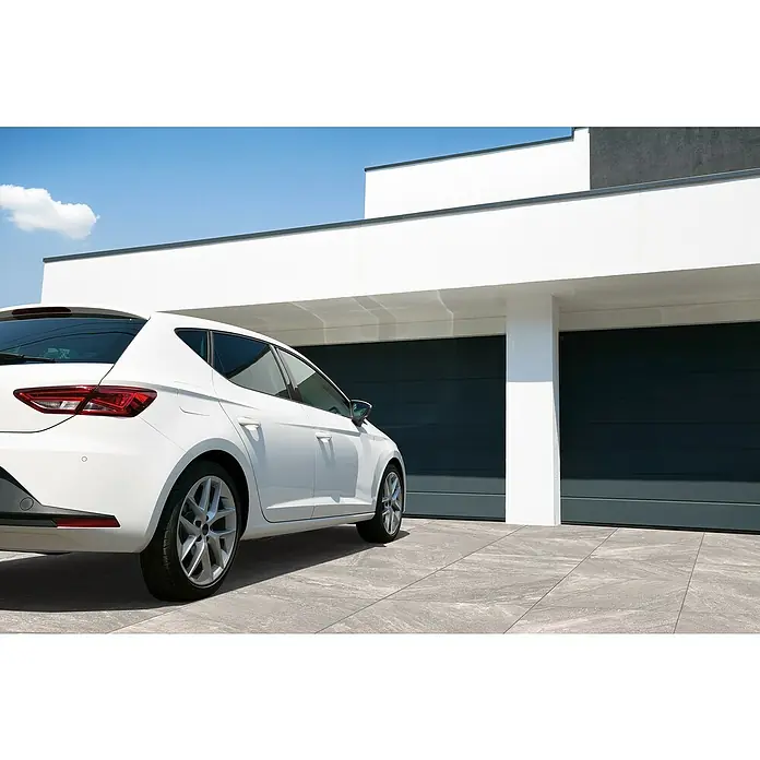 Terrassenfliese Quarzo Tortora - 60 x 60 x 2 cm, Grau/Braun, Matt - Ein weißes Auto parkt vor einer modernen Garage mit zwei grauen Garagentoren unter einem strahlend blauen Himmel.
