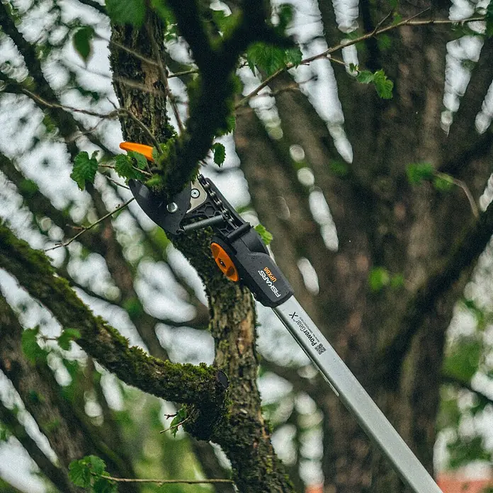 Fiskars Teleskop-Schneidgiraffe UPX86 - Max. Aststärke: 32 mm - Nahaufnahme einer Fiskars PowerGear X Astschere UPX86 beim Beschneiden eines Baumes, Fokus auf Präzision und Effizienz im Garten.
