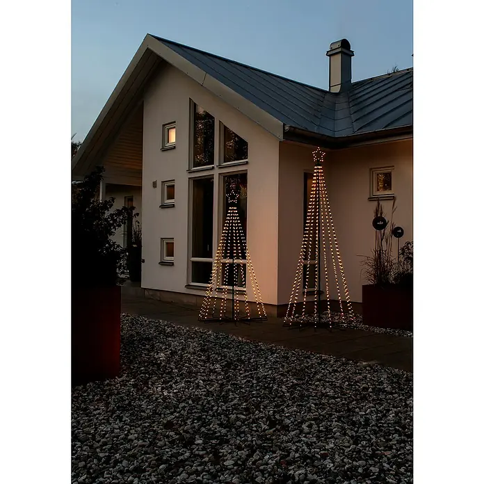 Konstsmide LED-Weihnachtsleuchte Tannenbaum - Höhe: 180 cm, Anzahl Leuchtmittel: 515 Stk. - Zwei leuchtende Weihnachtsbaumdekorationen vor einem modernen Haus, die festliche Stimmung verbreiten. Die Bäume strahlen warmes Licht aus.