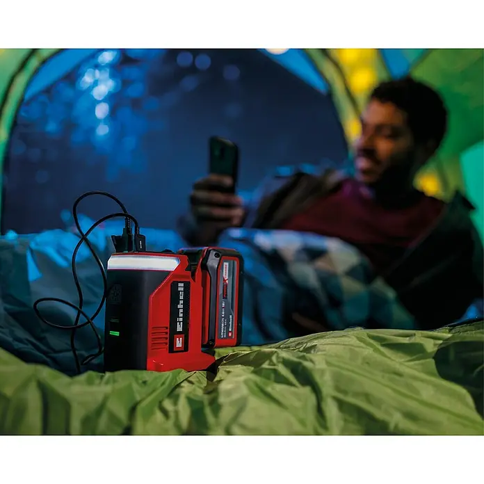 Einhell Power X-Change 18V Akku-Energiestation TE-ES 18/150/1 Li-C-Solo - 18 V, Ohne Akku - Ein Einhell Power X-Change Akku-Adapter mit Lampe, ideal zum Laden von Geräten beim Camping, im Fokus. Ein Mann benutzt sein Handy im Hintergrund.