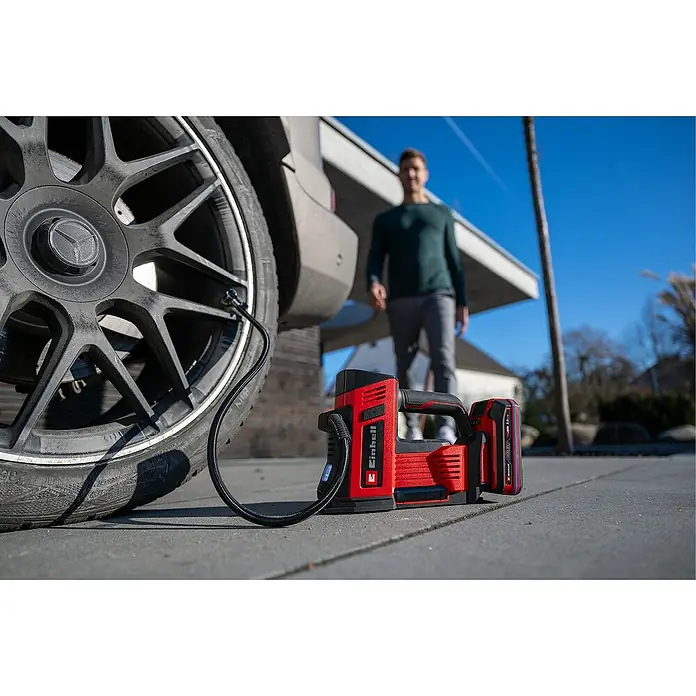 Einhell Power X-Change 18V Akku-Kompressor CE-CC 18/23 D Li-Solo - 18 V, Ohne Akku, 11 bar - Ein roter Einhell Akku-Kompressor neben einem Autoreifen, mit einem Mann im Hintergrund, ideal zum Aufpumpen von Reifen und anderen aufblasbaren Gegenständen.