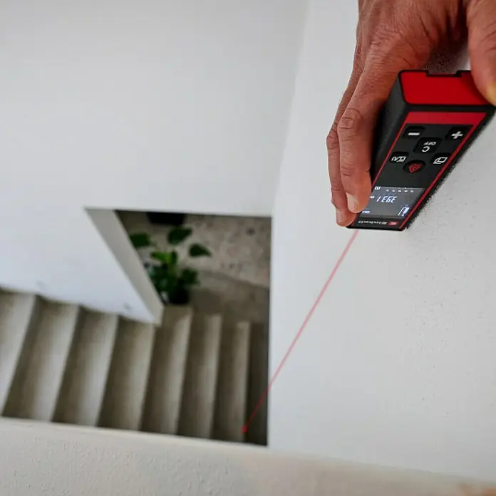 Einhell Laserentfernungsmesser TC-LD 60 R - Messbereich: 0,05 - 60 m, Ohne Batterien - Ein roter und schwarzer Entfernungsmesser wird verwendet, um mit einem roten Laserstrahl einen Treppenabsatz zu messen.