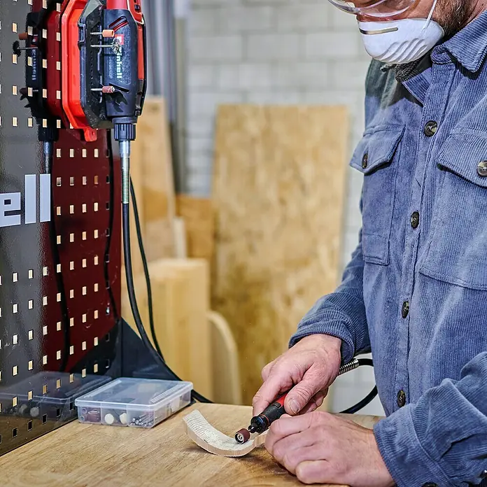 Einhell Schleif- & Gravurwerkzeug - 150 W, 10.000 U/min - 35.000 U/min - Bild eines Mannes, der mit einem Einhell Multifunktionswerkzeug ein Werkstück bearbeitet. Das Werkzeug ist an einer Werkbank befestigt.