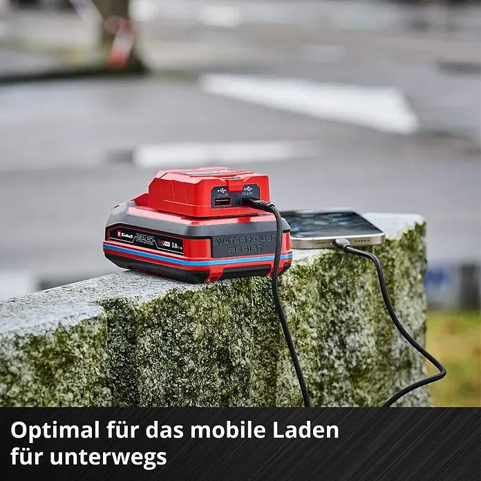 Einhell Power X-Change 18V USB-Akku-Adapter TC-CP 18 Li - 18 V - Ein Einhell Power X-Change Akku-Adapter lädt ein Smartphone im Freien. Der Adapter ist rot und schwarz und als mobile Ladestation optimal.