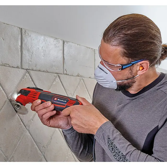 Einhell Elektro-Multifunktionswerkzeug TE-MG 350 EQ - 350 W, Sonstige - Mann benutzt ein Einhell Multifunktionswerkzeug, um an Fliesen zu arbeiten, mit Schutzbrille, Atemschutzmaske und Gehörschutz.