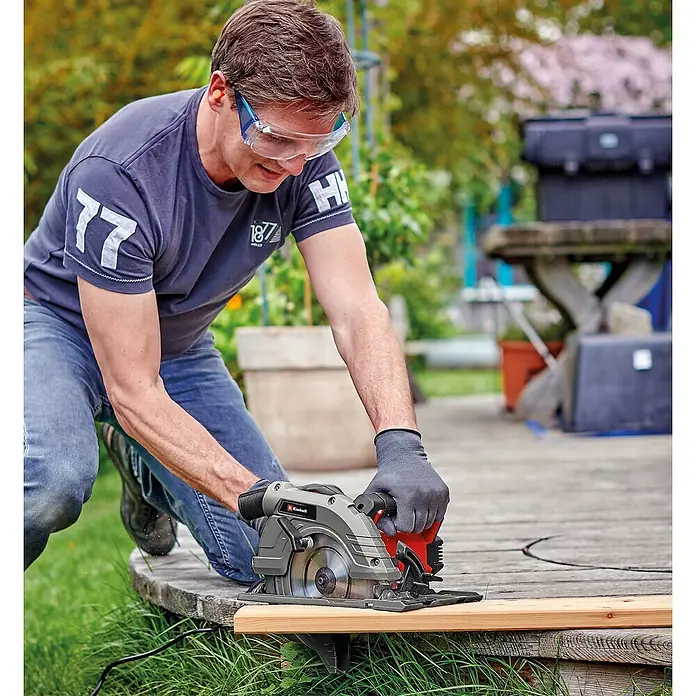 Einhell Handkreissäge TE-CS 190/1 - 1.500 W, Durchmesser Sägeblatt: 190 mm, Schnitttiefe bei 90 °: 66 mm - Ein Mann sägt ein Holzbrett mit einer Einhell-Kreissäge im Freien, wobei er Schutzbrille und Handschuhe trägt.