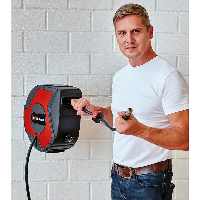 Einhell Druckluftschlauchtrommel TC-PH 150 - 15 m - Ein Mann mit einem Einhell Schlauchaufroller an einer weißen Backsteinmauer. Der Schlauchaufroller ist rot und schwarz.