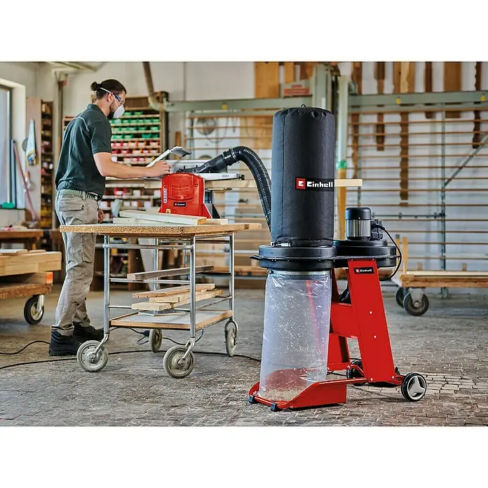 Einhell Absauganlage TE-VE 550/2 A - 2.400 W, Staubbeutelvolumen: 65 l - Staubabsauganlage Einhell im Einsatz in einer Werkstatt, mit einem Handwerker und Holzbearbeitungsgeräten im Hintergrund.