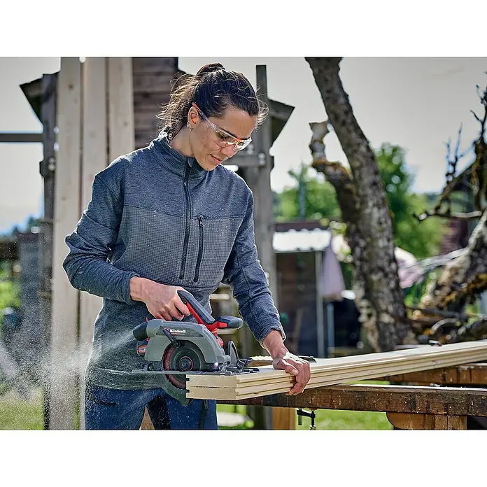 Einhell Power X-Change 18V Akku-Handkreissäge TP-CS 18/165 Li BL - Solo - 18 V, Ohne Akku, Durchmesser Sägeblatt: 165 mm, 5.000 U/min - Eine Frau sägt Holz mit einer Einhell Akku-Handkreissäge. Die Säge ist rot und grau und wird zum Zuschneiden von Holz verwendet.