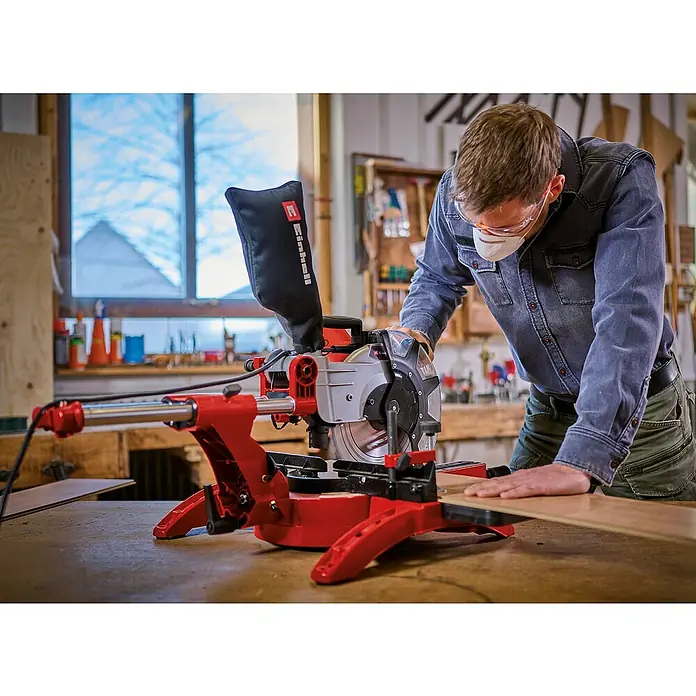 Einhell Kappzugsäge TC-SM 2534/1 Dual - 2.350 W, Durchmesser Sägeblatt: 250 mm, Leerlaufdrehzahl: 4.000 U/min - Eine Einhell Kapp- und Gehrungssäge im Einsatz, mit einem Handwerker, der Holz schneidet und dabei Schutzbrille und Maske trägt.