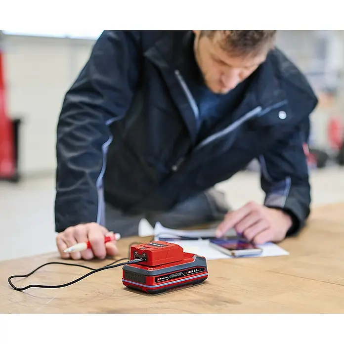 Einhell Power X-Change 18V USB-Akku-Adapter TC-CP 18 Li - 18 V - Ein Mann benutzt einen Akkuadapter. Der Adapter ist rot und schwarz. Er wird verwendet, um ein Smartphone aufzuladen.