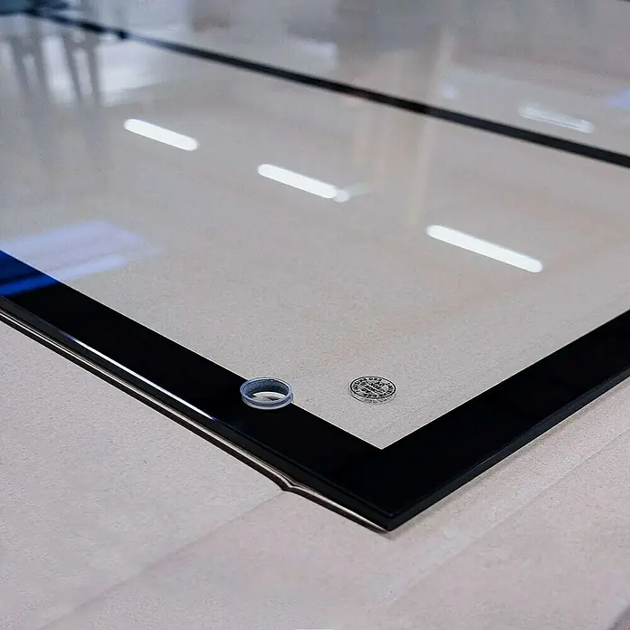 Inova Glasschiebetür Klarglas Komplettset 5 Felder schwarz inkl. Softclose -  - Nahaufnahme einer schwarzen Glasplatte mit einem transparenten Ring und einem kleinen runden Aufkleber, die die hochwertige Verarbeitung hervorhebt.