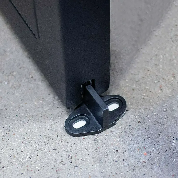 Inova Glasschiebetür Stahl Satiniert Komplettset 3 Felder Kickplatte schwarz inkl. Softclose - Satiniertes Glas - Nahaufnahme eines schwarzen Türfeststellers aus Kunststoff an einer Tür, der auf einem Betonboden montiert ist.