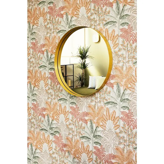 Papel pintado Botánico Palmeras - Beige, Floral, 10 x 0,53 m - Un espejo redondo dorado cuelga en una pared con un patrón de hojas exóticas, reflejando la habitación.