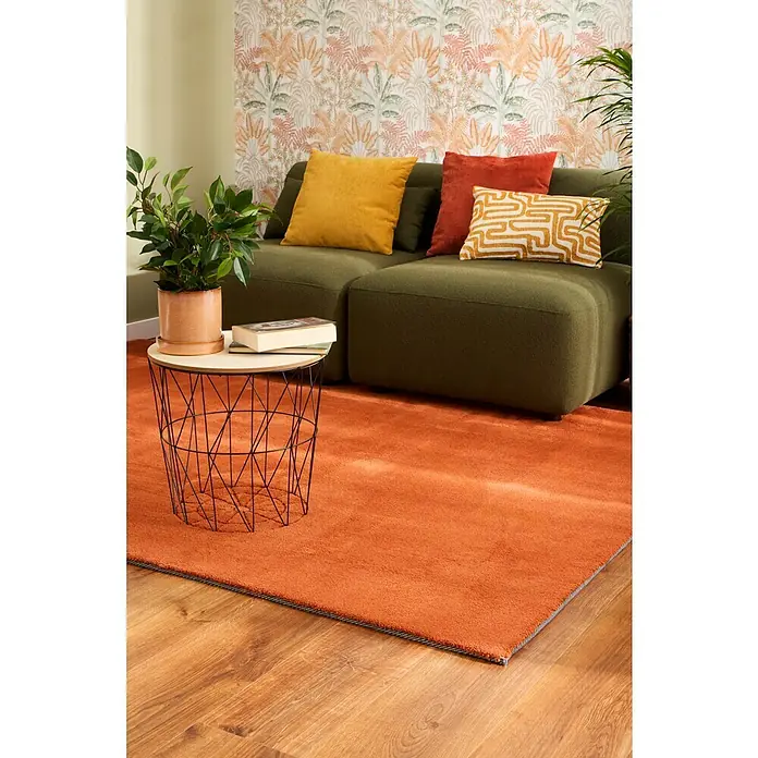 Papel pintado Botánico Palmeras - Beige, Floral, 10 x 0,53 m - Primer plano de una sala de estar con una alfombra naranja, un sofá verde y una mesa auxiliar con una planta.