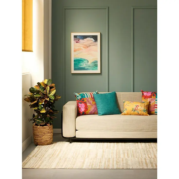 Montó Bricolovers Pintura para paredes EcoNatura - Verde Sueño, Mate, 4 l - Una sala de estar acogedora con un sofá beige, cojines coloridos, una pintura abstracta y una planta en maceta en una cesta para un interior confortable.