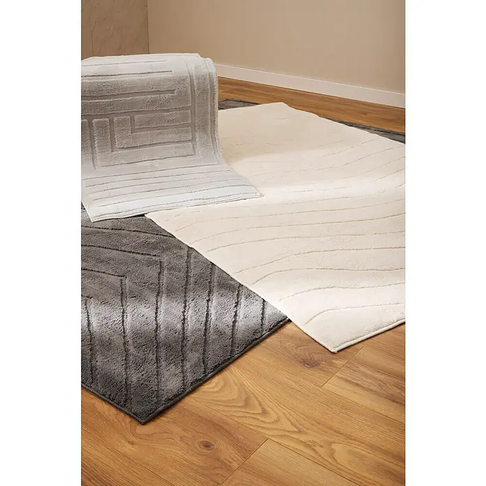 Alfombra de pelo corto Stelvio Cuadros - Plata, 230 x 160 cm, 100% Poliéster - Tres alfombras de baño diferentes en tonos grises y crema con diferentes patrones sobre un suelo de madera.