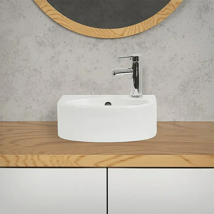 LuxeBath Aufsatzwaschbecken Waschschale Oval Weiß Spülbecken Aufsatzwaschtisch - 25,5 x 33,5 cm, Ohne Spezialglasur, Weiß - Aufsicht auf ein modernes, weißes Waschbecken mit Chromarmatur auf einer hellen Holzplatte mit weißem Unterschrank und Spiegel.
