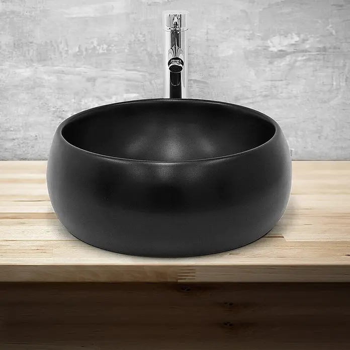 LuxeBath Aufsatzwaschbecken Waschtisch aus Keramik für Badezimmer / Gäste-WC - Ohne Spezialglasur, Schwarz - Eine moderne, schwarze Aufsatzwaschbecken-Keramikschale mit glatter Oberfläche, die auf einer Holzplatte und vor einer Betonwand steht.