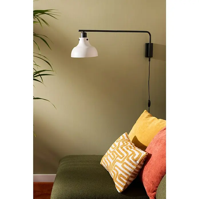 swingcolor Pintura para paredes - Verbena, Mate, 4 l - Este primer plano muestra una lámpara blanca de pared con un brazo negro, ubicada sobre un sofá adornado con almohadas.