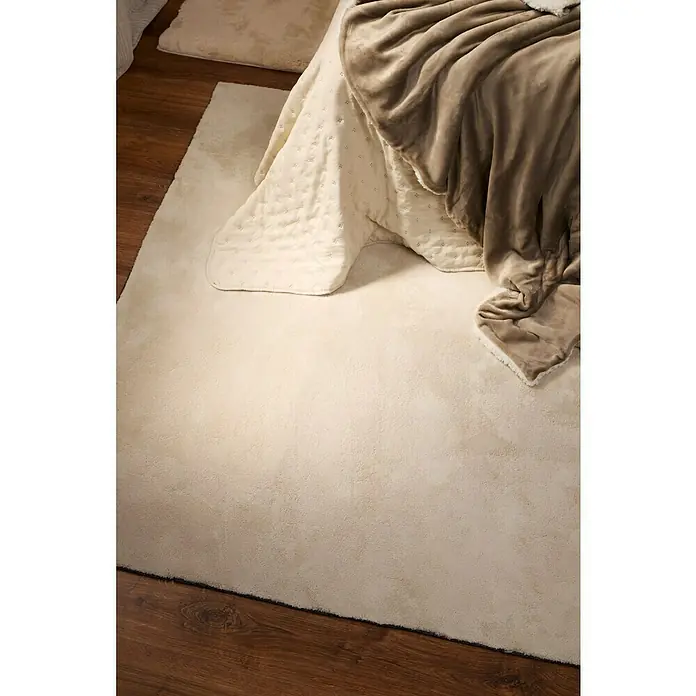 Edredón Corinto - 180 x 260 cm, Poliéster, Arena - Una alfombra esponjosa de color crema sobre un suelo de madera debajo de una colcha con una manta beige.