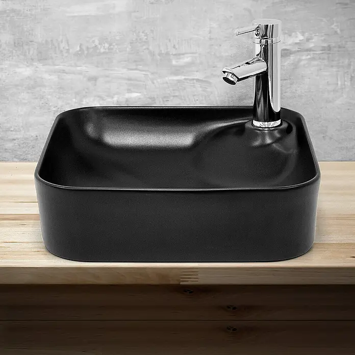LuxeBath Aufsatzwaschbecken Waschtisch aus Keramik für Badezimmer / Gäste-WC - Ohne Spezialglasur, Schwarz - Elegantes schwarzes Waschbecken mit modernem Chromhahn auf einer hellen Holzoberfläche vor einem grauen Hintergrund.