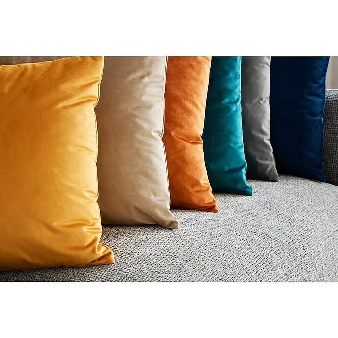 Cojín Velvet - 45 x 45 cm, Textil, Yema - Fila de cojines de terciopelo de colores amarillo, beige, naranja, verde azulado, gris y azul marino sobre un sofá gris texturizado.