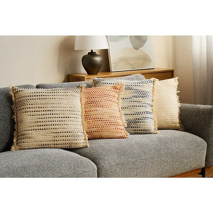 Cojín Dakira - 45 x 45 cm, Textil, Natural, Cuadrado - Fila de cojines decorativos con flecos en varios colores en un sofá gris, creando un ambiente acogedor y elegante en el espacio vital.