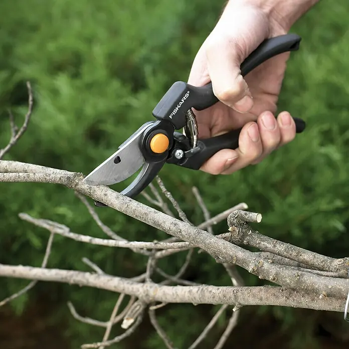 Fiskars Gartenschere Pro P90 - Bypass, Max. Aststärke: 26 mm - Nahaufnahme einer Hand, die mit einer Fiskars-Gartenschere einen Ast beschneidet, vor einem grünen Hintergrund.