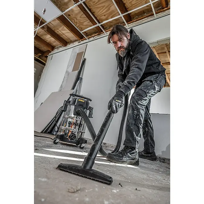 DeWalt Elektro-Nass- & Trockensauger DXV30SAPTA - 1.050 W, Behältervolumen: 30 l, Filterreinigung: Vollautomatisch - Ein Mann benutzt einen Dewalt Staubsauger auf einer Baustelle, um den Boden zu reinigen, wobei der Fokus auf dem Staubsauger liegt.