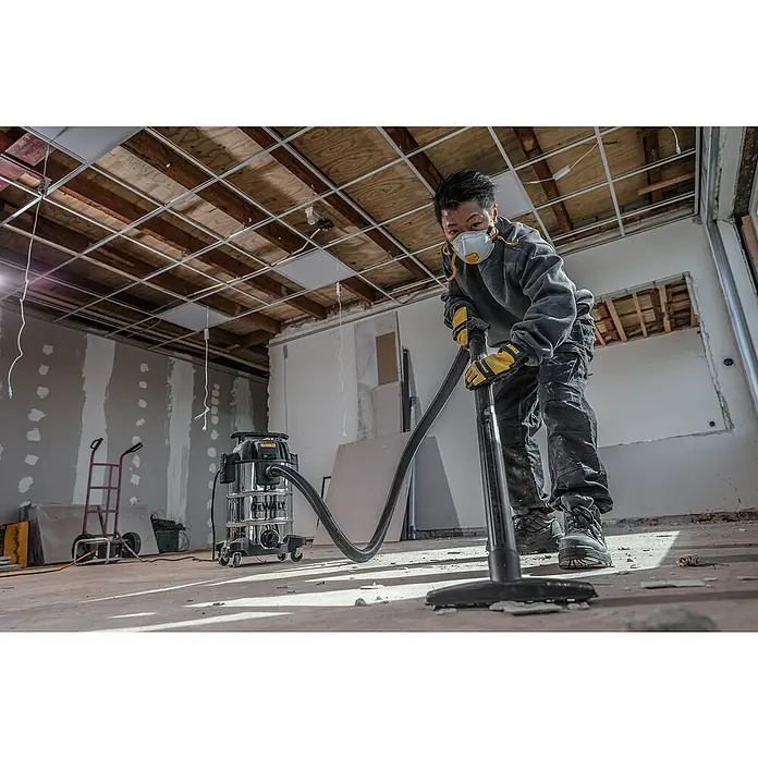 DeWalt Elektro-Nass- & Trockensauger DXV30SAPTA - 1.050 W, Behältervolumen: 30 l, Filterreinigung: Vollautomatisch - Ein Handwerker verwendet einen DeWalt Staubsauger, um in einem unfertigen Raum mit freiliegender Decke und Trockenbauwänden Staub und Schmutz zu entfernen.