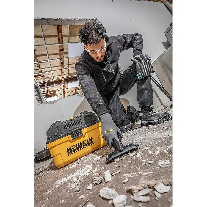 DeWalt Elektro-Nass- & Trockensauger DXV23G - 230 W, Behältervolumen: 23 l - Ein Bauarbeiter benutzt einen gelben DeWalt Staubsauger, um Schutt auf einer Baustelle zu beseitigen. Persönliche Schutzausrüstung wird getragen.