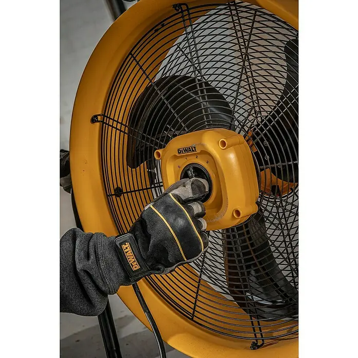 DeWalt Bodenventilator DXF2067 - 110 W, Max. Luftleistung: 102,2 m³/h - Ein gelber, industrieller Ventilator der Marke DeWalt wird von einer Hand mit Arbeitshandschuh bedient, um die Geschwindigkeit einzustellen.